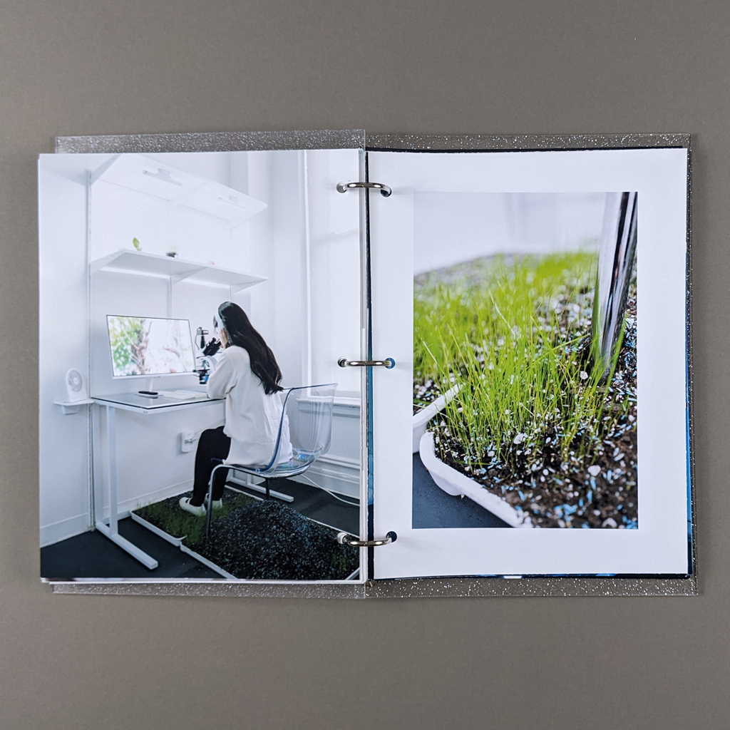 "You are the star" inside spread. Verso: full-bleed photo of a woman at a microscope. A computer monitor displays the microscope's view. Trays of soil grow grass beneath the woman's chair. Recto: surrounded by a white border, a close-up photograph of grass growing beneath the chair.