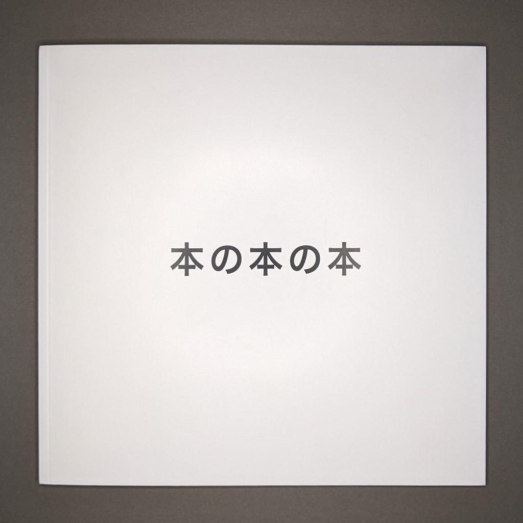 Front cover of "本の本の本": the title text is set in bold black type on a completely white background. The title is centered on the square, softcover book. 
