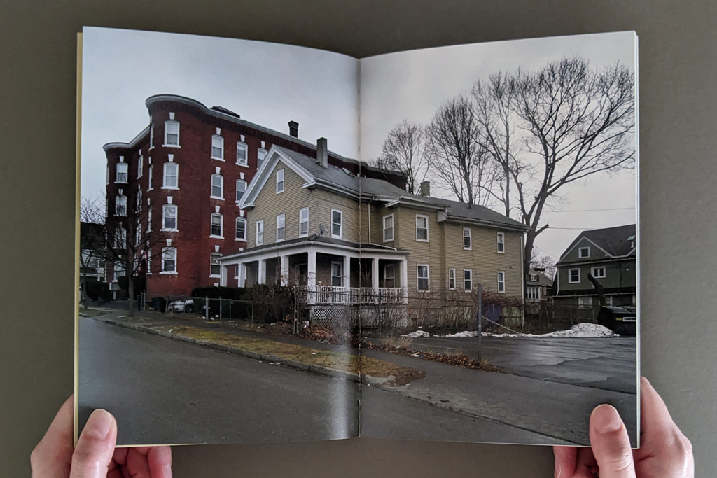 Pictures From the Outside, inside spread: full-bleed spread with a photo of a yellow house between an empty lot and a larger apartment building